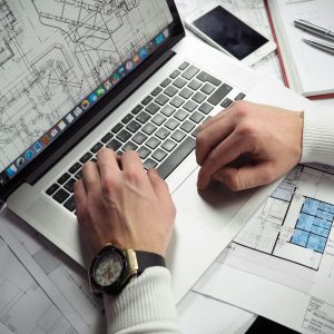 Home Architect reviewing detailed floor plans and schematics on a laptop with a smartphone nearby.